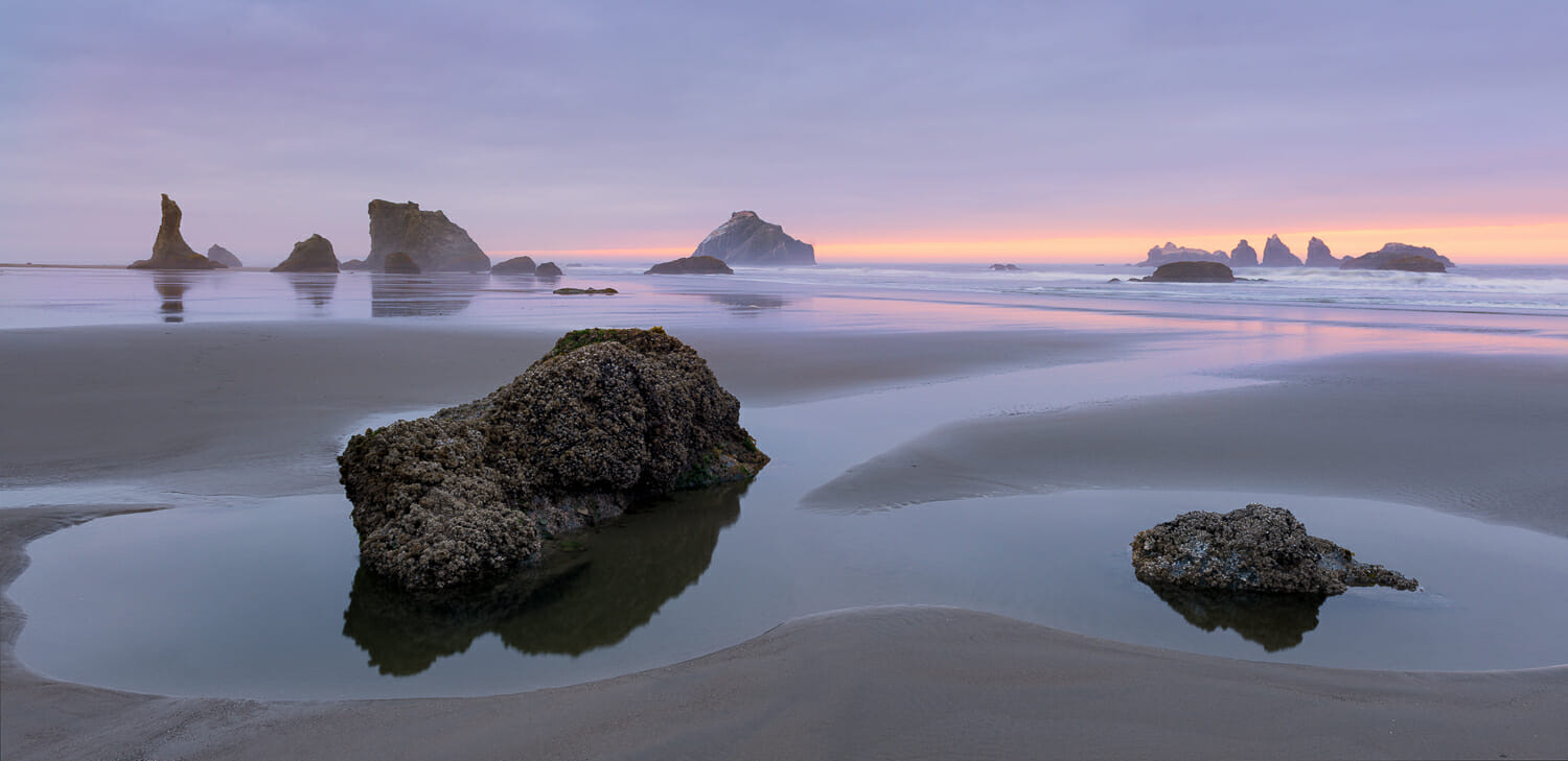 Rocks on the sand at low tide during a pink sunset at Bandon Beach