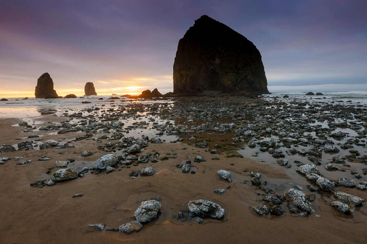 Cannon beach at sunset with rocks scattered across the sand