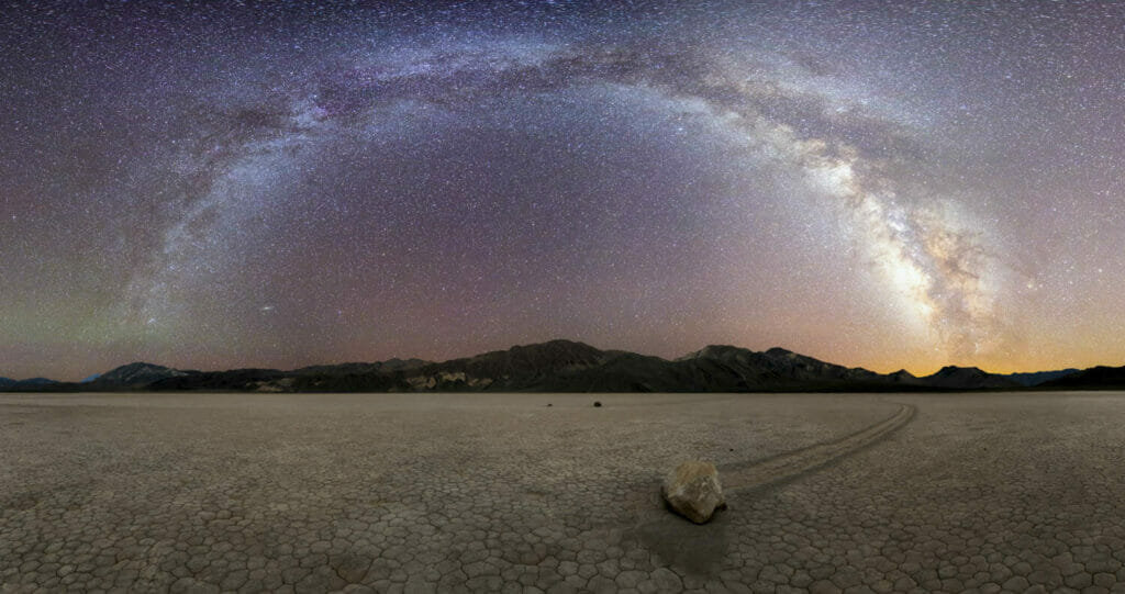 The milky way arches above a rock at the racetrack playa in death valley, usa