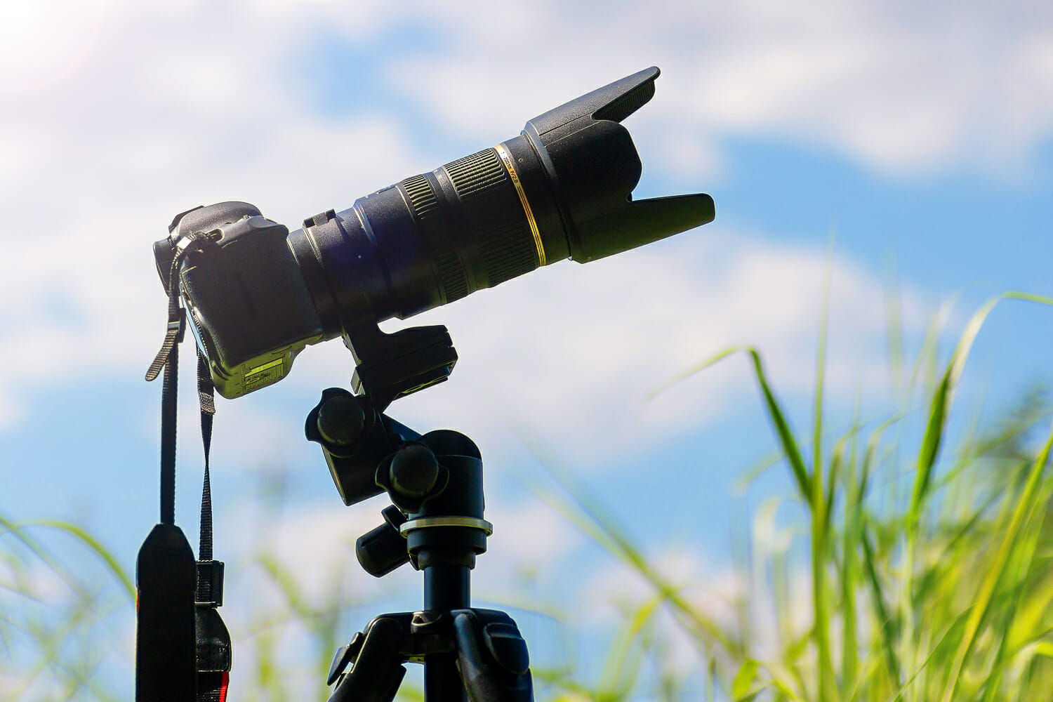 Dslr camera with a telephoto lens mounted on a tripod outdoors under a sunny sky.