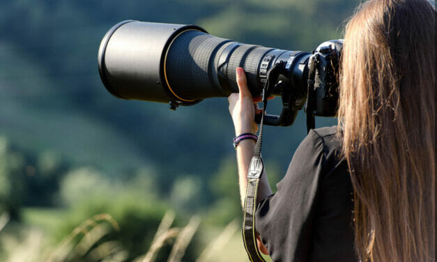 Photographer with a long lens camera capturing images outdoors.