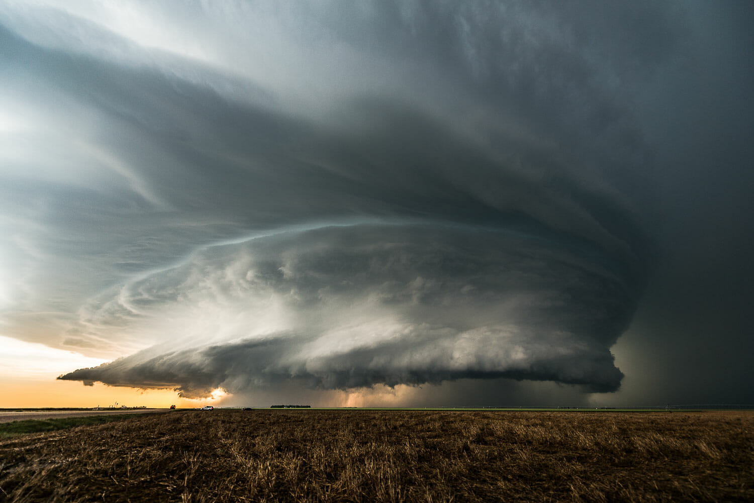 A massive supercell thunderstorm looms over open plains at sunset.