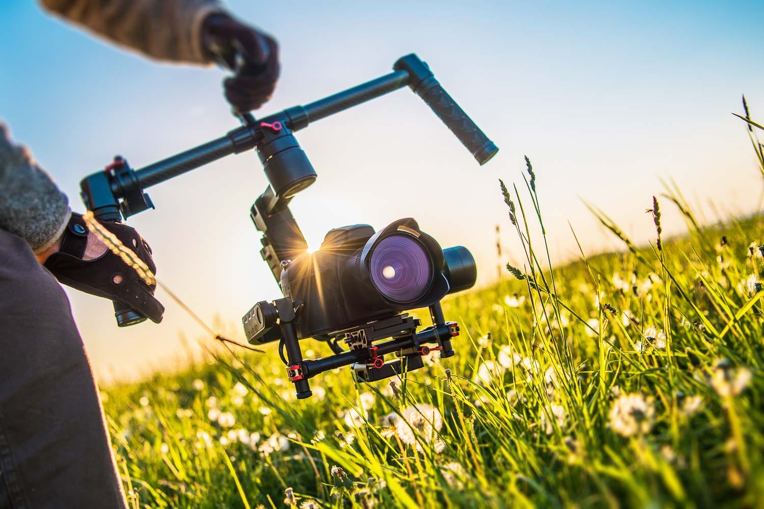 A filmmaker operating a camera on a stabilizing gimbal during a field shoot at sunset.