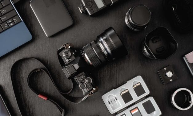 Assorted photography equipment arranged on a dark surface, including a camera, lenses, and memory cards.