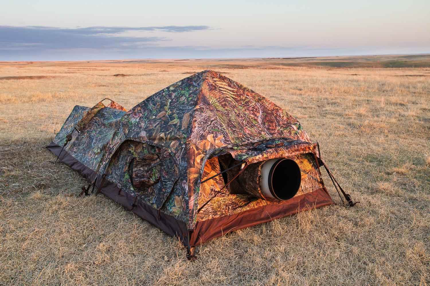Camo-patterned tent set up in a grassy field at dusk.
